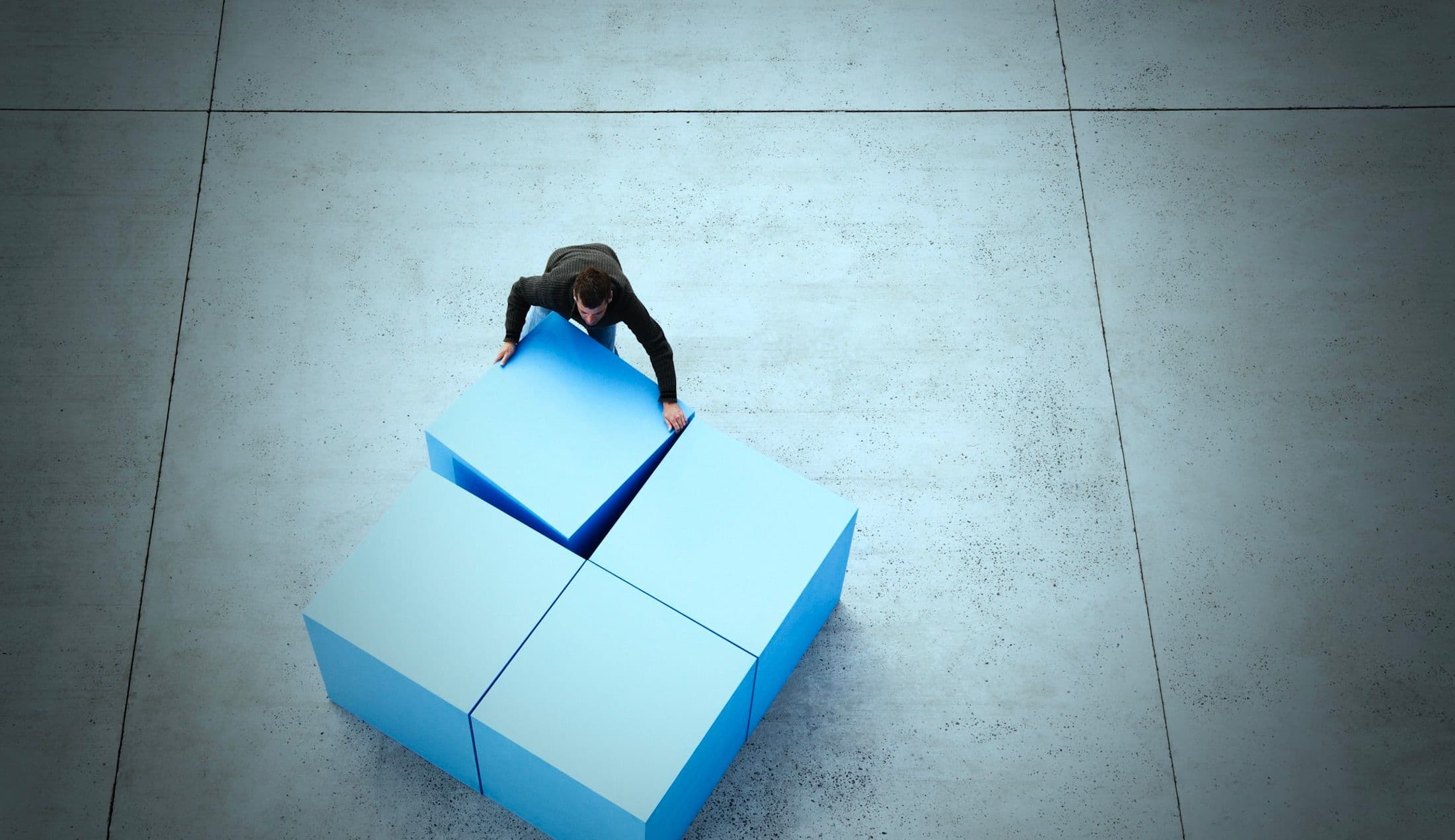 A photo of a businessman, seen from above, shoving four massive cubes together