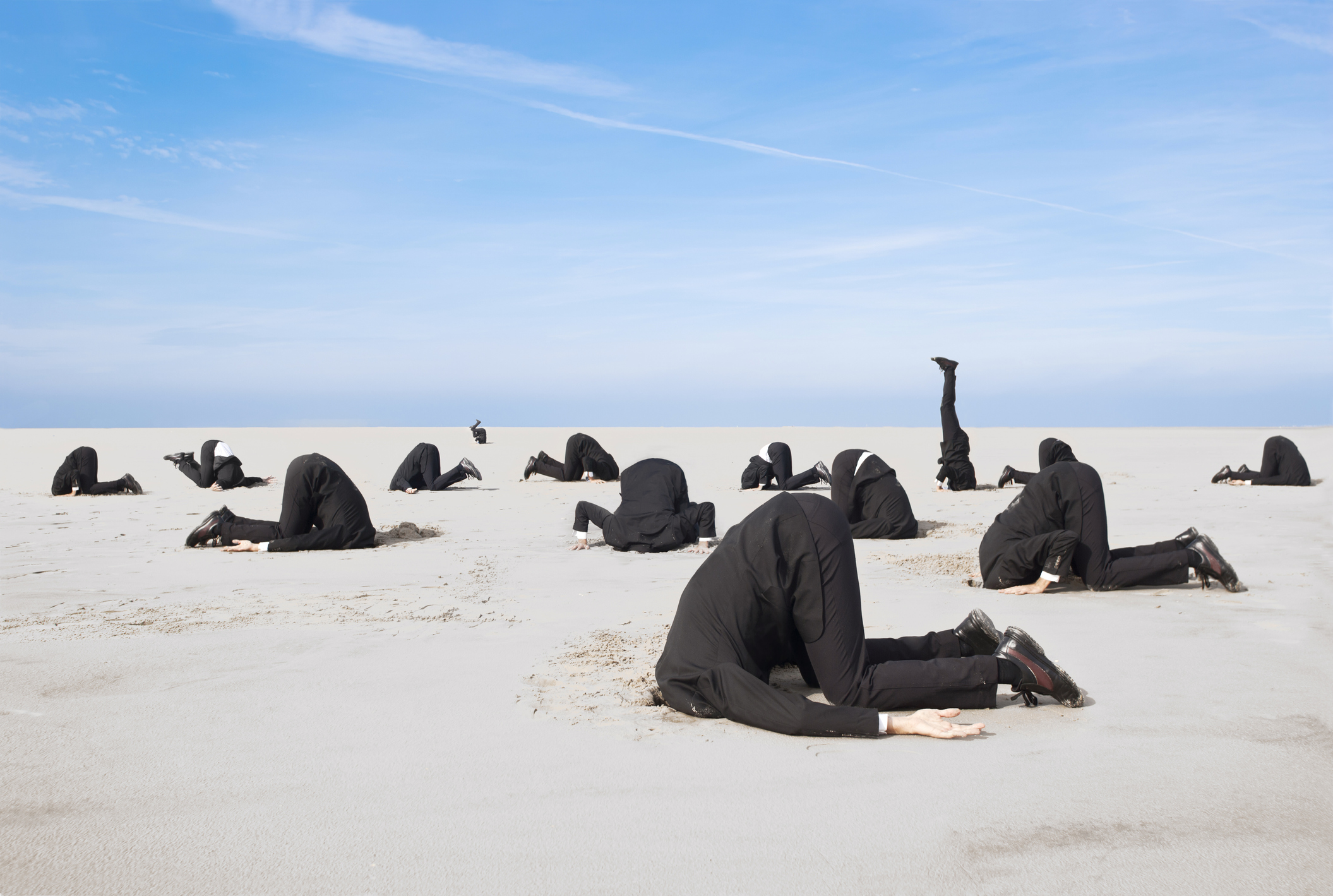 A photo of executives in suits with their head stuck in the desert sand.