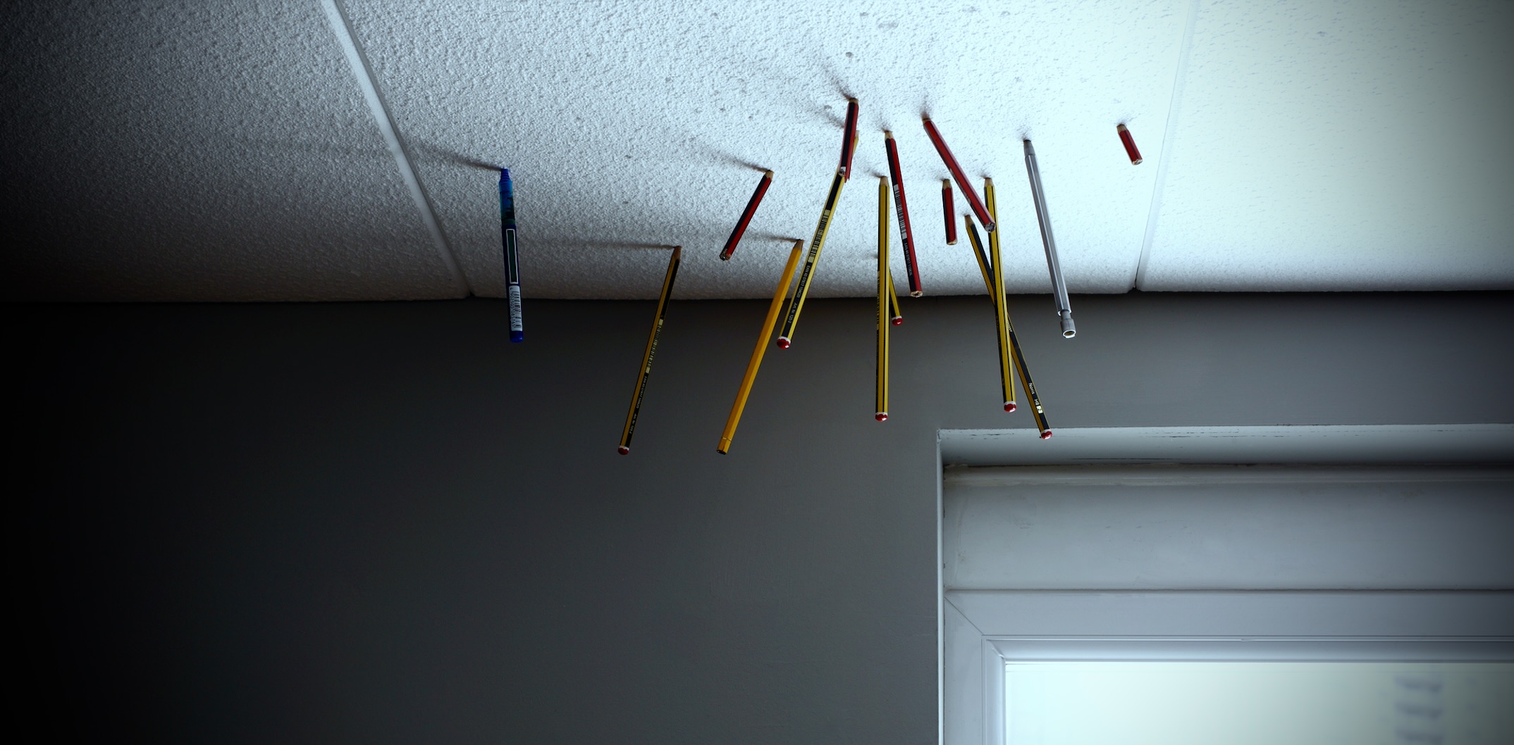 A photo of pencils stuck in bland Styrofoam office ceiling tiles.