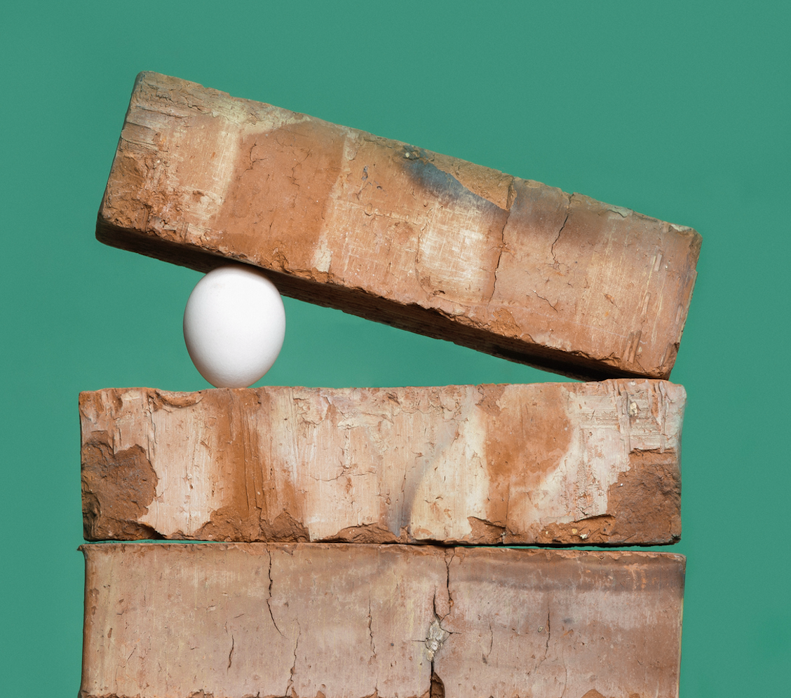 An egg sits wedged between bricks against a green background.