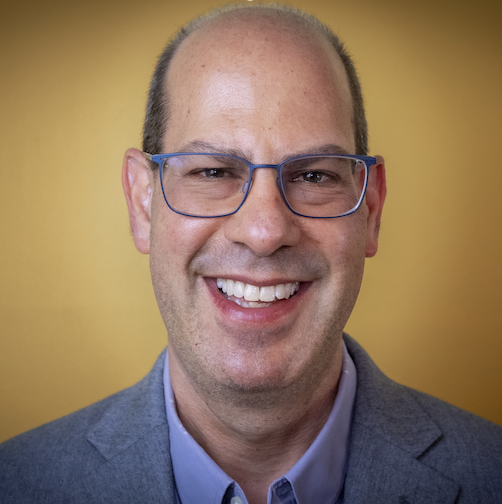 Photo of a middle-aged White man with glasses, a blue-gray jacket and a wide smile.