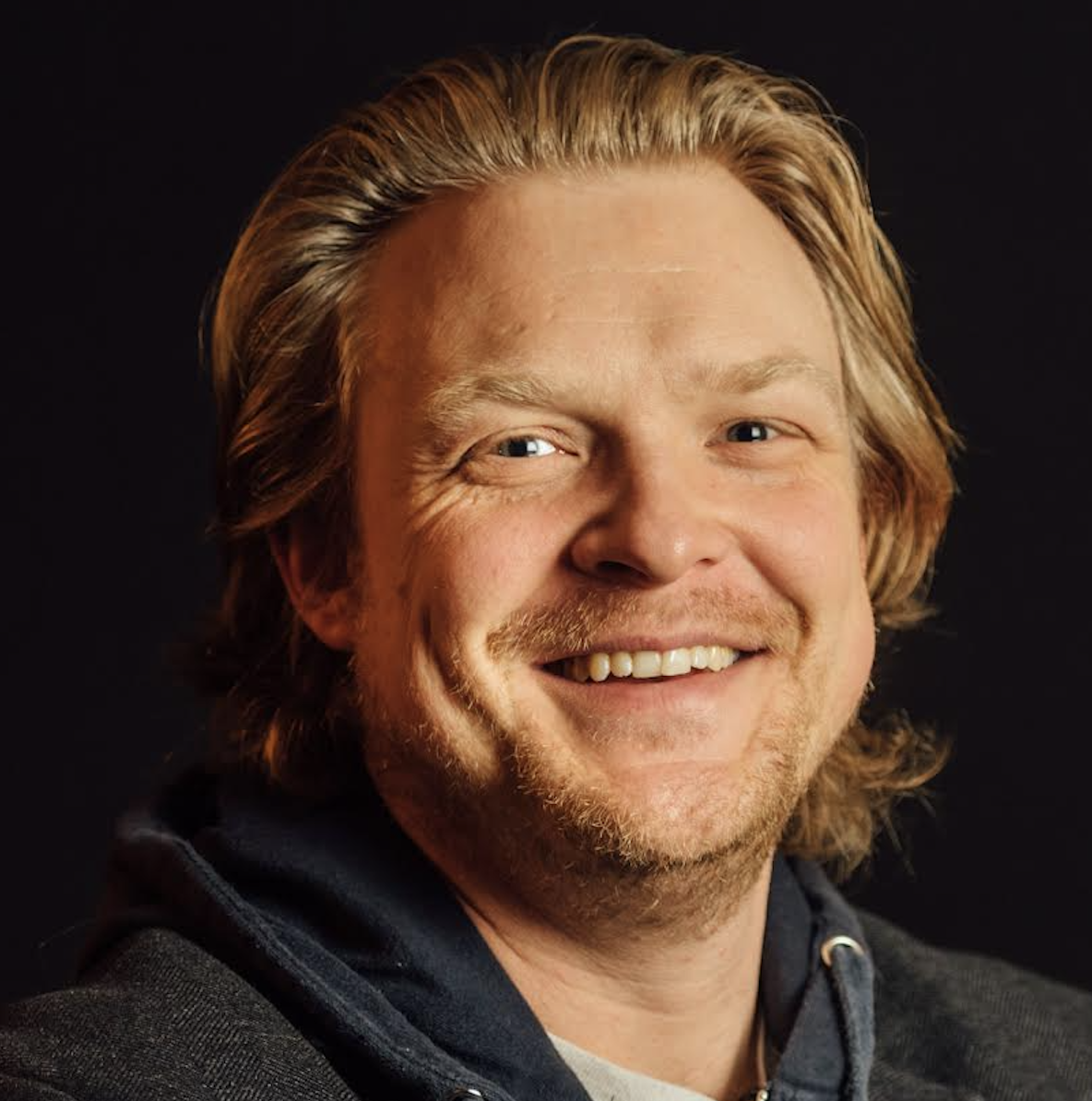 Photo of a white man in a hoodie with long blonde hair dusting the back on his neck.