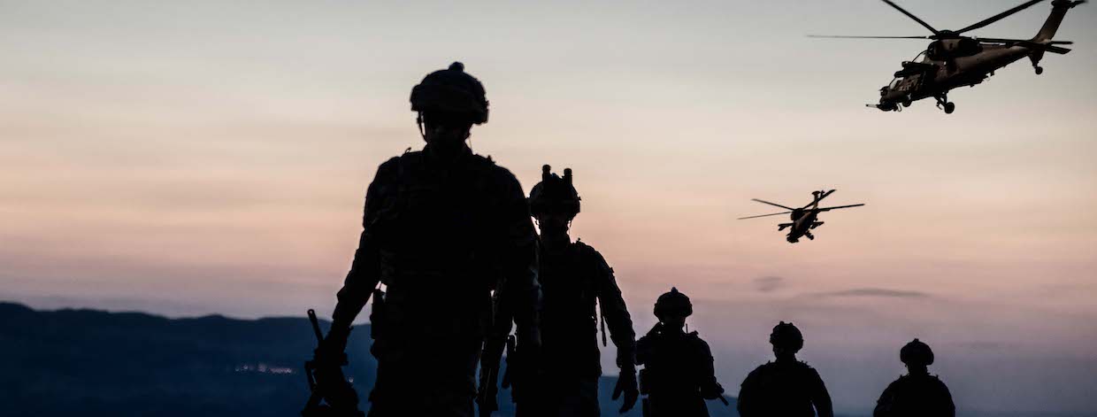 silhouette of soldiers walking as two helicopters fly in the distance